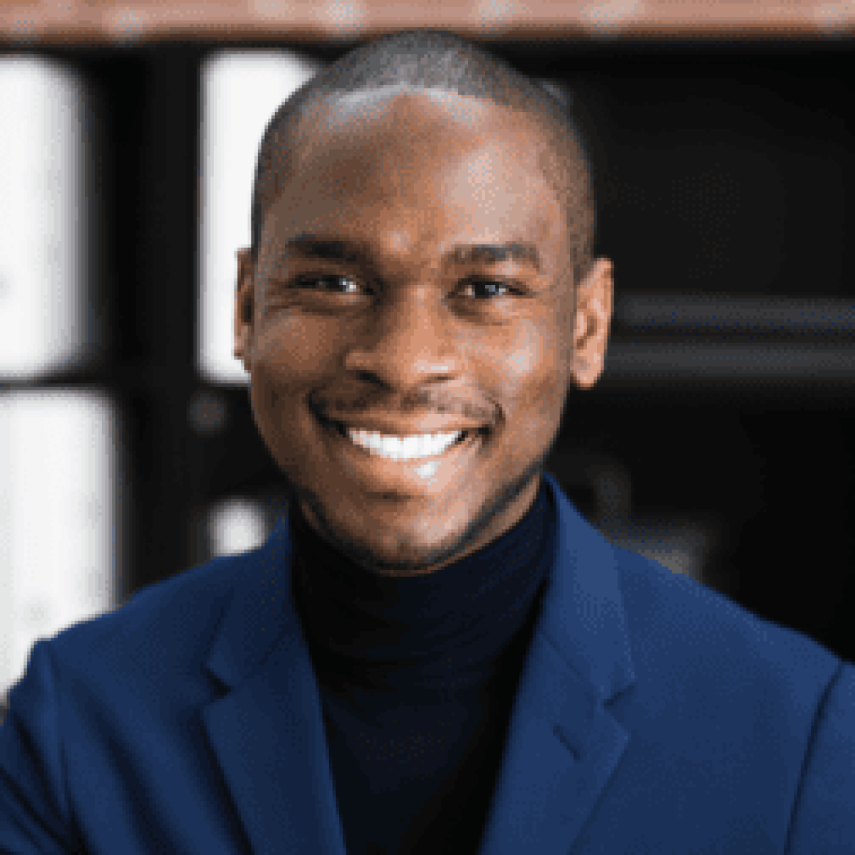 A person in a blue blazer smiles in front of shelves with binders.